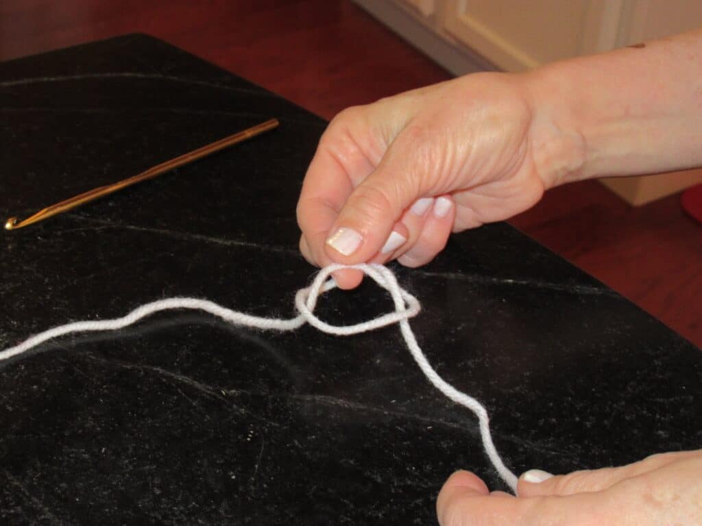 Looping white yarn with two hands to begin forming a slipknot