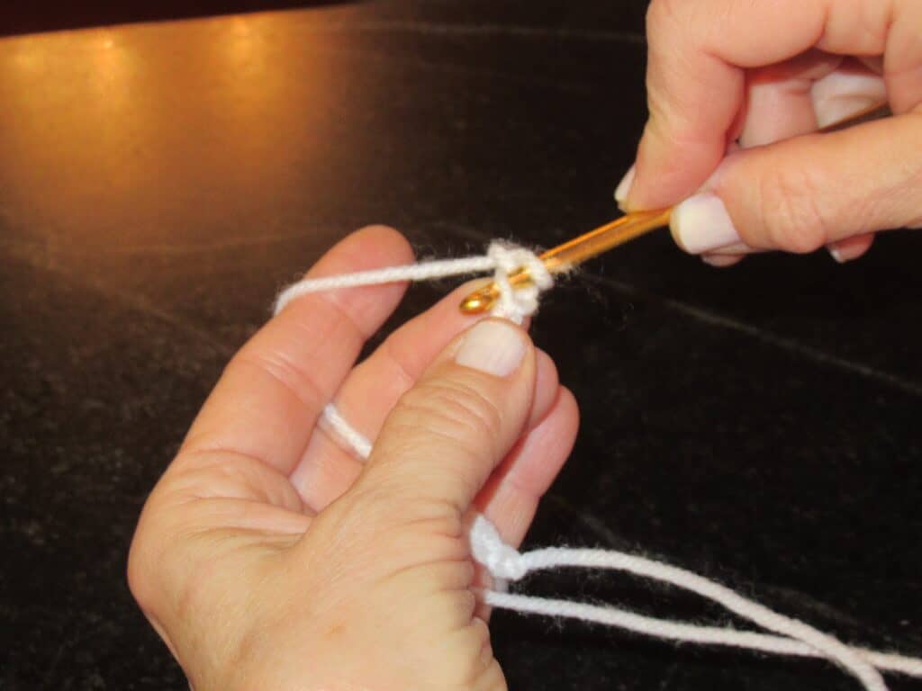 Single crochet step one inserting gold crochet hook into white yarn loop two hands