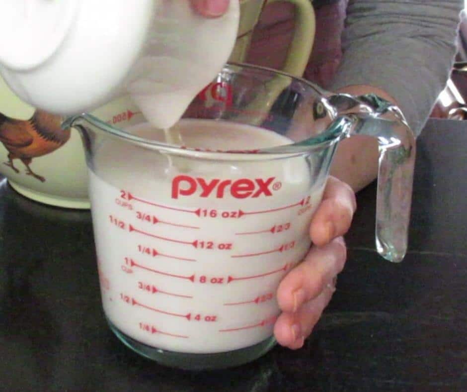 Pouring vinegar from white pitcher into 2 cup measuring cup of almond "milk"